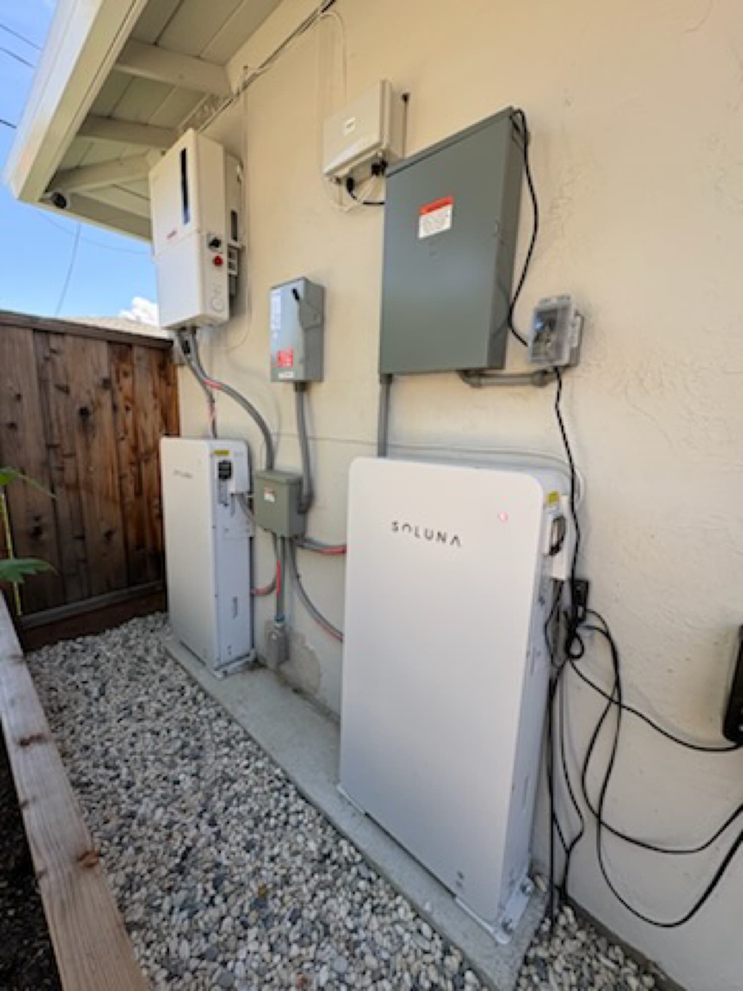 Solar inverter and a Soluna home battery with sub-panel on an exterior wall — solar-plus-storage backup by Astral Electrical, NEC 705.